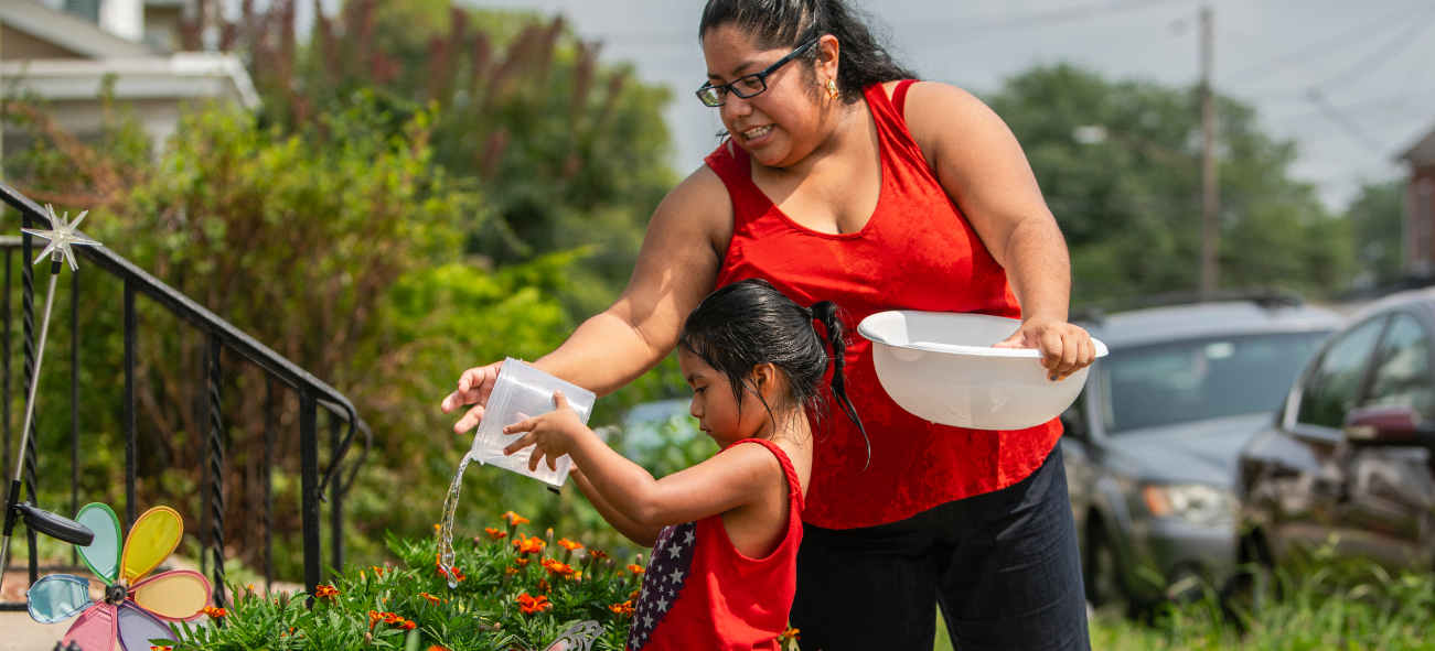 Latino mother and daughter outside home watering flowers